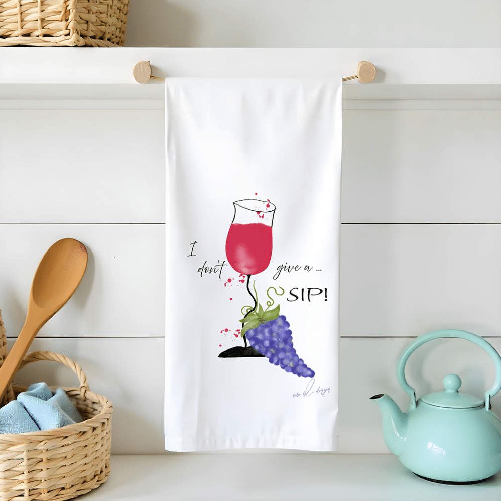 I don't give a sip flour sack tea towel features a crooked glass of red wine spilling onto a bunch of purple grapes at the bottom on the glass.