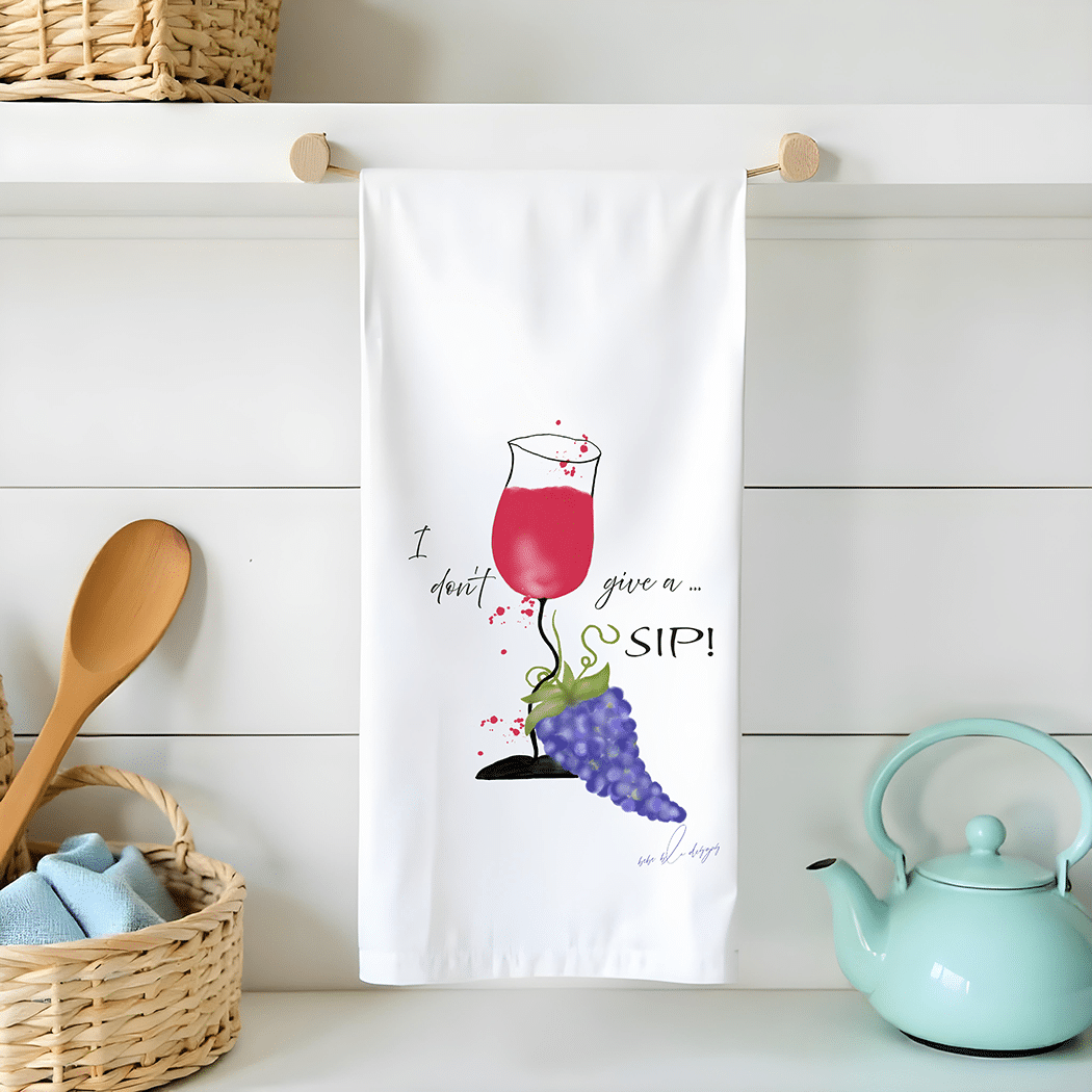 I don't give a sip flour sack tea towel features a crooked glass of red wine spilling onto a bunch of purple grapes at the bottom on the glass.