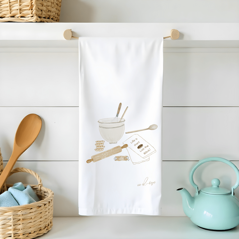 lick the bowl flour sack tea towel features a mixing bowl, wooden spoon, rolling pin and a tea towel that say "Life is short, Lick the Bowl"
